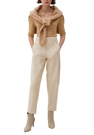 Kvinde iført beige bukser med høj talje, tan tætsiddende top med 3/4 ærmer, tan sweater hængt over skuldrene, og beige ankelstøvler med hæl.