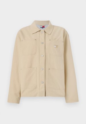 Veste en toile beige avec un col pointu, fermeture à boutons sur le devant, deux poches poitrine et un petit logo en patch. Texture douce et design ajusté.