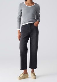 Camisa gris de manga larga con cuello blanco, combinada con pantalones vaqueros negros de cintura alta con bajos deshilachados y zapatos beiges con cordones.