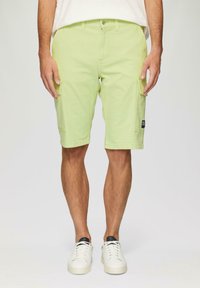 Jasnozielone szorty cargo z kieszeniami bocznymi, zapięciem na guziki i podwiniętymi nogawkami. W komplecie z białymi trampkami i beżową koszulą.