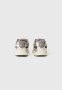 Grå og krem sneakers med mesh og metalliske detaljer. Har polstret krage og teksturert såle. Bakfra, som viser logodetaljer.