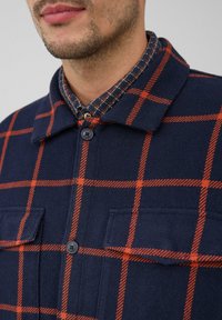 Marineblauwe wollen blend shirtjacket met een oranje ruitpatroon, voorzien van een knoopkraag, twee voorzakken en een gestructureerde afwerking.