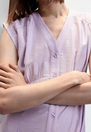 Lavender mouwloze blouse met een V-hals, stof heeft een subtiele glans, vooraan knoopsluiting en lichte plooien op de schouders.