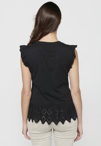 Top en coton noir avec des manches courtes à volants et un ourlet festonné brodé. Texture lisse avec des motifs découpés complexes en bas.
