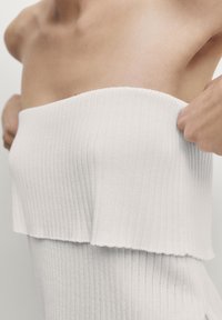 Top bianco a righe senza spalline, con un design a strati in un tessuto testurizzato. L'orlo è leggermente sfilacciato e aderisce perfettamente al corpo.