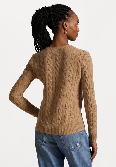 Pull en tricot à mailles torsadées de couleur brun clair, avec un ourlet côtelé et des manches longues. La texture est douce avec un motif en relief.