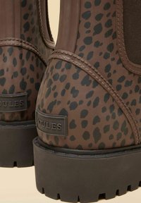 Bruine rubberen laarzen met zwarte luipaardprint, een gestructureerd oppervlak, elastische zijpanelen en een stevige zwarte zool met opvallend profiel.