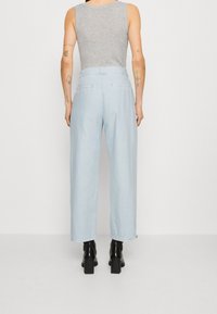 Hellblaue weite Hosen mit hoher Taille, aus einem weichen Stoff, mit hinteren Taschen und kombiniert mit schwarzen High Heels Stiefeln.