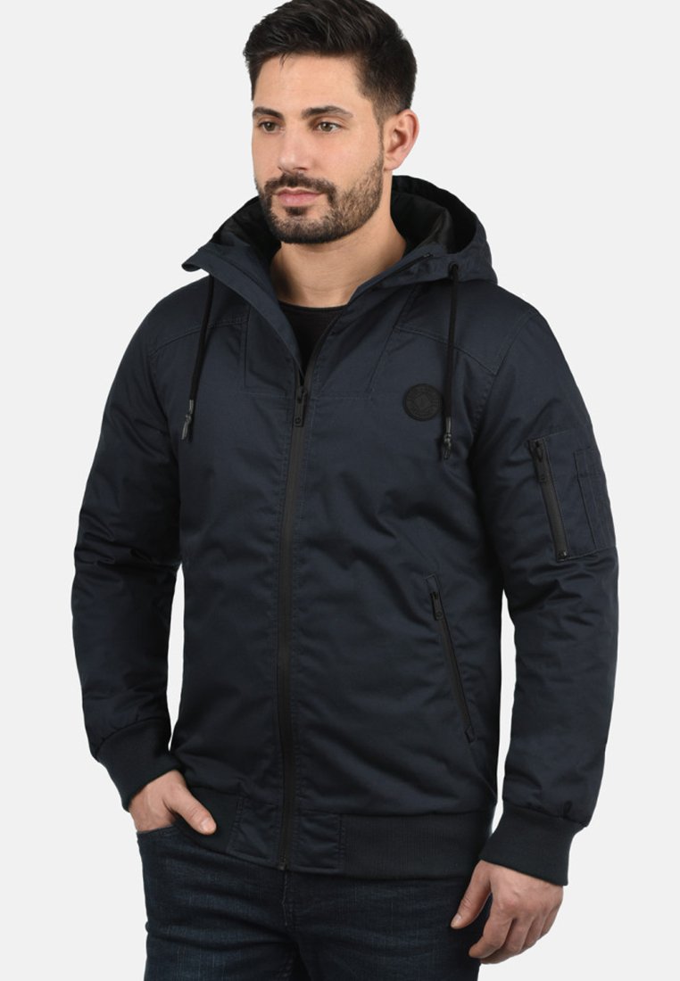 Navyblauwe hoodie met ritsluiting, zijzakken en gestructureerde stof. Beschikt over elastische manchetten en een patch op de bovenste linkerkant van de borst.