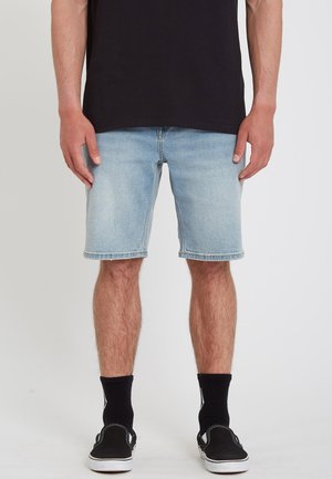 Hellblaue Denim-Shorts mit geradem Schnitt, ausgefranstem Saum und Fünf-Taschen-Design, kombiniert mit schwarzen Knöchelsocken und schwarzen Sneakers.