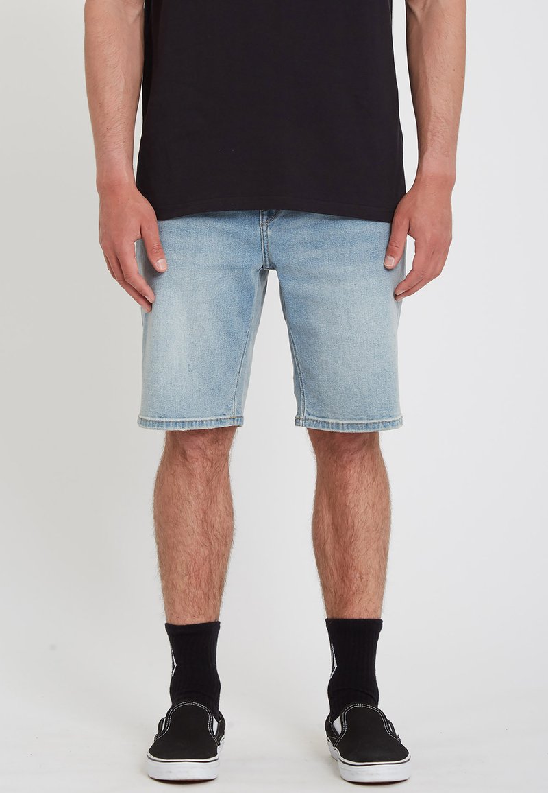 Light blue denim shorts with a straight cut, frayed hem, and five-pocket design, paired with black ankle socks and black sneakers.