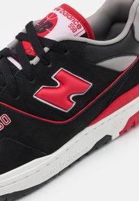 Sneaker nera in camoscio con dettagli rossi e logo, dotata di linguetta imbottita e intersuola bianca con marchio; suola in gomma testurizzata.