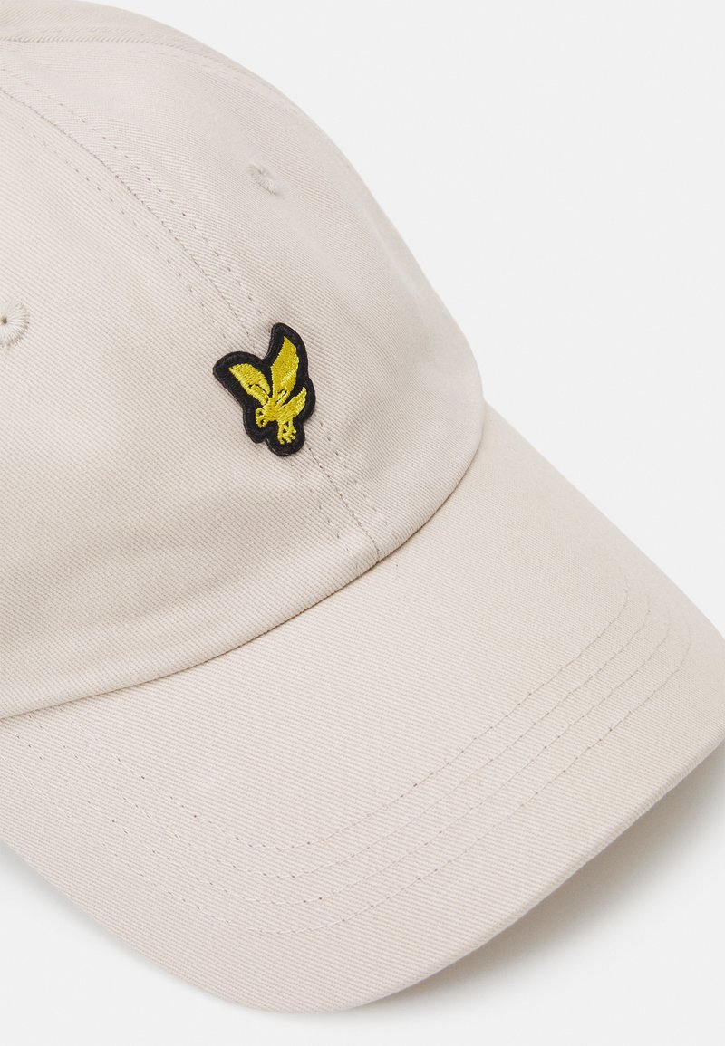 Cappello beige in cotone con una superficie testurizzata. Presenta un logo di farfalla gialla ricamato sul lato sinistro anteriore.