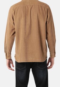 Bruine corduroy blouse met lange mouwen, met knoopmanchetten en zijsplitten. Textuurstof en een relaxte pasvorm, gezien van achteren.