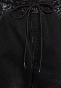 Svarta denim-joggers har en elastisk midjeband med dragsnöre, metallictips och sidofickor, och har en slät, texturerad finish.