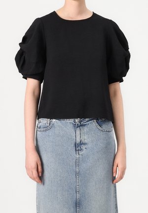 Top noir court en tissu texturé, avec des manches bouffantes et un col rond, assorti à une jupe en denim bleu clair.