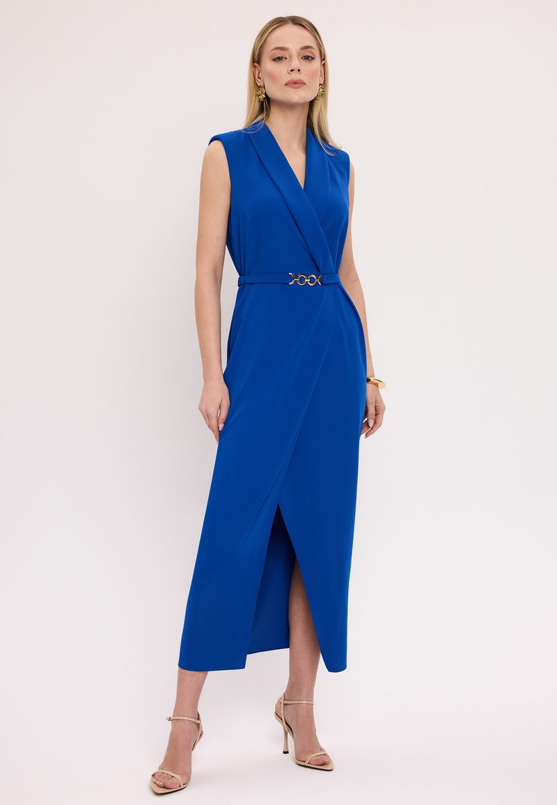 Niebieska sukienka bez rękawów z krojem kopertowym, z złotym paskiem w talii i rozcięciem z przodu, wykonana z gładkiego materiału.