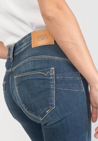 Mörkblå denimjeans med en figursydd design, med en distinkt läderlapp på baksidan och kontrasterande sömmar på fickorna.