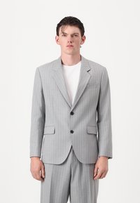 Gray pinstriped suit jacket with notch lapels, two buttons, and front pockets, worn over a white t-shirt, featuring a tailored fit.