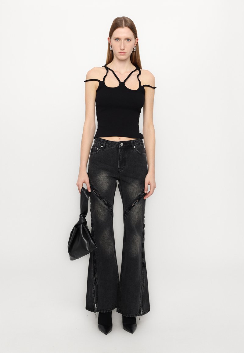 Top corto nero a righe con spalle scoperte abbinato a jeans neri svasati con fessure laterali e una finitura lucida. Borsa nera e tacchi.