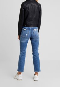 Svart läderjacka, ljusblå slitna denimjeans och vita sneakers; synliga rivna detaljer på jeansen och fickorna.