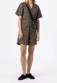 Leopardprint korte jumpsuit met korte mouwen, knoopsluiting en zijzakken. Gecombineerd met een zwarte schoudertas en zwarte sneakers.