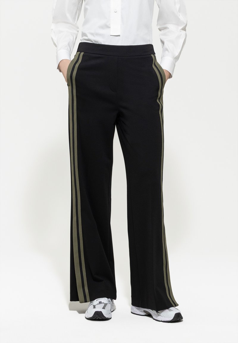 Schwarze weite Hosen mit olivgrünen Streifen an den Seiten, aus weichem Material, mit einem bequemen elastischen Bund.