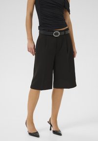Zwarte cropped broeken met een riem, met een slanke textuur en stijlvol ontwerp. Gecombineerd met zwarte puntige hakken.