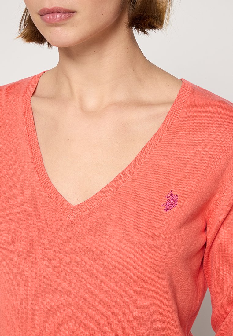 Koraleowy sweter w serek wykonany z miękkiej, teksturowanej tkaniny; z małym fioletowym logo na klatce piersiowej; dopasowany krój.