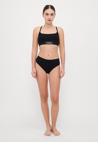 Melnās bikini komplekts, kas satur cropped topu ar regulējamiem siksniņām un logotipu, kopā ar augstām biksēm. Gluda, elastīga auduma.