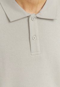 Világosszürke poloing texturált felülettel, standard gallérral, két gombos zárással és rövid ujjakkal.