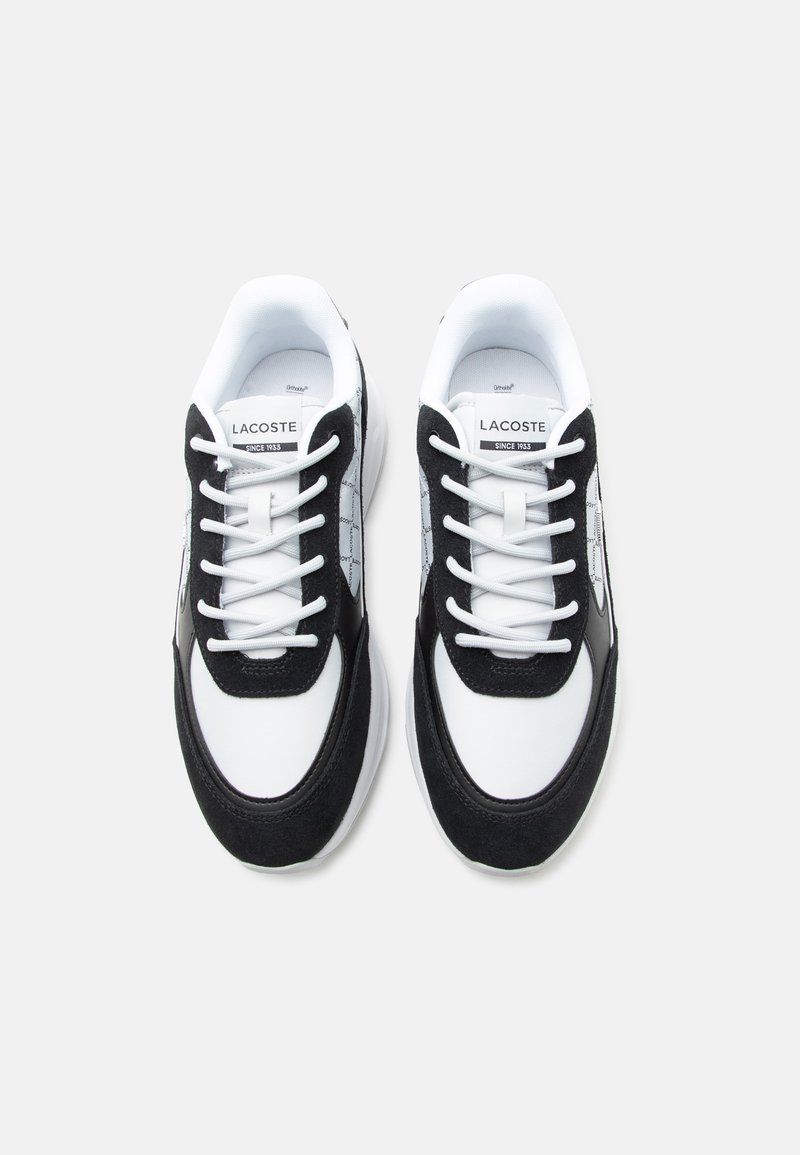 Coppia di sneaker Lacoste bianche e nere con lacci bianchi, etichetta del marchio visibile sulla linguetta, posizionate affiancate su uno sfondo bianco.