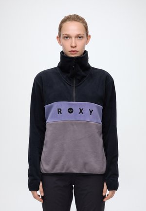 Un mannequin est de face et porte une polaire ROXY noire, lavande et grise, avec une fermeture éclair au quart, un col montant et une poche avant.