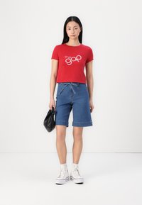 Rode cropped t-shirt met het logo "the gap", gecombineerd met denim bermuda shorts. Witte sneakers en een zwarte handtas maken de outfit compleet.