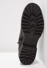 Svart ankelsko med en strukturerad gummisula, utrustad med djupa sulor, sid dragkedja och en slät läderöverdel. Storlek 37 synlig på sulan.