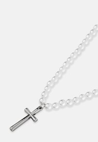 Pērļu kaklarota ar sudraba krusta piekariņu. Kaklarota sastāv no vienāda izmēra baltām pērļu virknēm un pulēta metāla krusta, kas kalpo kā izceļošs elements.