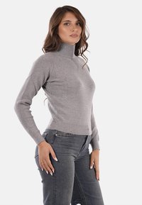 Maglione grigio a collo alto con texture a coste, vestibilità slim e maniche lunghe. Indossato con jeans alti e scuri, che mettono in risalto una silhouette elegante.