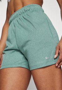 Vihreät heather-tyyliset Nike-shortsit, joissa on joustava vyötärö, pienellä hopeisella logolla vasemmassa alalaidassa ja sileä pinta.