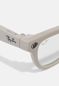 Ray-Ban-briller i lys grå plastik med klare linser, et fremtrædende logo på stangen og et lille kameralinse på siden.