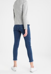Blazer grigio aderente con dettagli delle cuciture, abbinato a jeans skinny blu scuro con orli sfilacciati e sneakers bianche.