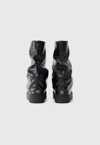 Bottines noires en cuir avec un design froncé, une surface texturée et une semelle en caoutchouc noir solide. Présente un petit logo sur le talon.