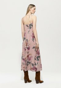 Blumenmuster Chiffonkleid in zartem Rosa mit dünnen Trägern, zeichnet sich durch ein fließendes Design und einen mittellangen Saum aus. Kombiniert mit braunen Stiefeletten mit Absatz.
