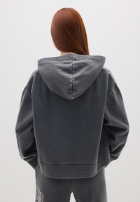 Felpa corta grigio scuro in tessuto morbido con un ampio cappuccio. Presenta spalle abbassate e polsini a coste. Abbinata a pantaloni della tuta coordinati.