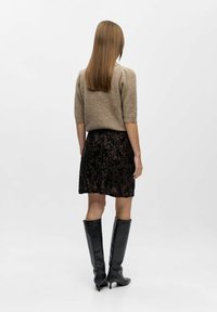 Beige gebreide trui met korte mouwen, gecombineerd met een zwarte pailletten minirok en kniehoge zwarte haklaarzen, gezien van achteren.