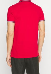 Rotes Polohemd mit klassischem Kragen, versehen mit navy- und weißen gestreiften Akzenten. Hergestellt aus glattem Stoff, figurbetontem Schnitt und kurzen Ärmeln.