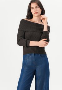 Brown ribbed off-the-shoulder sweater with three-quarter sleeves, paired with high-waisted blue denim wide-leg pants.