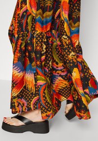 Farverig mønstret maxikjole med sorte, orange, blå og grøn nuancer samt et lagdelt design. Sorte platform sandals med bred rem.
