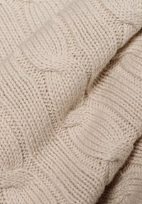 Beiger Strickstoff mit einem strukturierten Kabelmuster und gerippten Akzenten. Das Garn ist dick und weich und zeigt filigrane Nähdetails.