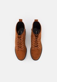 Bottines en daim marron avec lacets, bout rond, fermeture éclair latérale et semelle en caoutchouc. Doublure en toile à l'intérieur de la chaussure. Design minimaliste.