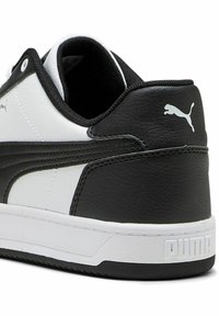 Mustvalge tenniseking, millel on tekstureeritud sünteetiline ülemine osa, polsterdatud krae ja kummitald. Omab Puma logo kandadel.